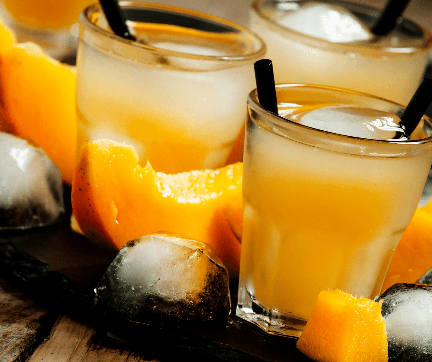 Mango Wodka in Long Drink Gläsern mit schwarzen Strohhalmen, Eiswürfeln und Mangowürfeln