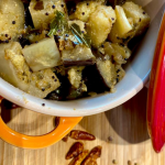 Geröstete Auberginen mit Curryblättern und Senfsamen in einem kleinen roten Tontopf angerichtet