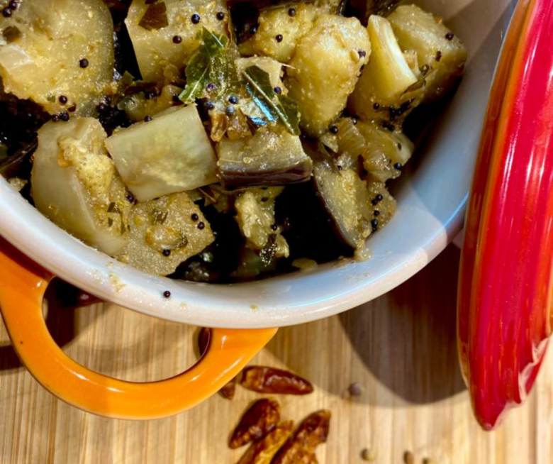 Geröstete Auberginen mit Curryblättern und Senfsamen in einem kleinen roten Tontopf angerichtet