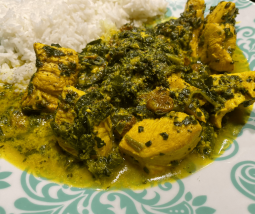 Leuchtend gelb-grünes Hähnchen Curry mit Sultaninen und Spinat. Angerichtet auf einem türkisen Teller mit weißem Basmatireis.
