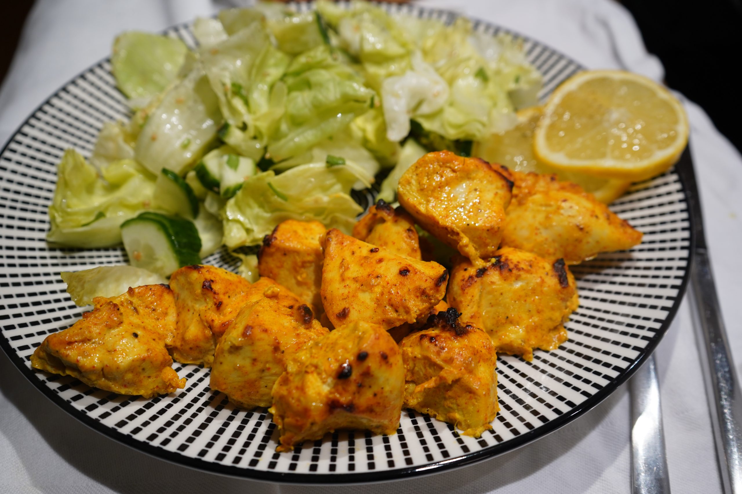 Saftiges Tandoori-Hähnchenfilet angerichtet mit Zitrone mit einem knackigen, grünen Salat.