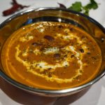 Dal Makhani in einer Kupferschale angerichtet mit Sahne-Swirls und frischen Methi-Blättern und etwas zerlassner Butter in der Sauce.