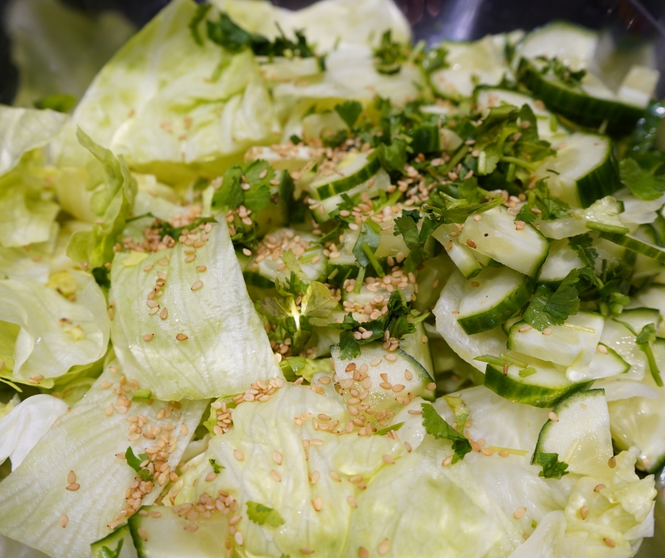 Nahaufnahme des Salates in der Schüssel: Eisbergsalat mit Salatgurke, frischem Koriander und geröstetem Sesam