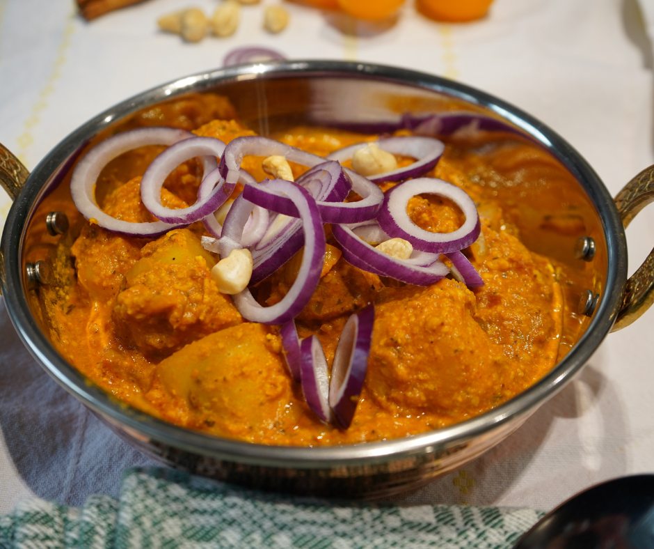 Cremiges Dum Aloo in einer Kupferschüssel angerichtet und mit Zwiebelringen garniert