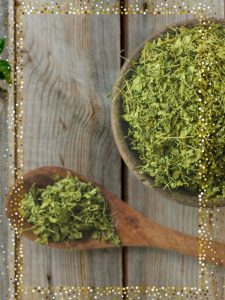 Kasuri Methi auf einem Löffel und in einer Schale, die auf einem Holztisch stehen. Das Bild hat einen Goldrahmen