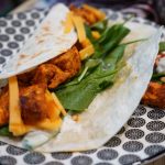 Saftiger Tandoori-Hähnchen-Wrap auf einem Teller angerichtet. Er ist gefüllt mit würzigem Tandoori-Hähnchen, Cheddar-Käse, Gurken-Joghurt-Sauce und Baby-Blattspinat