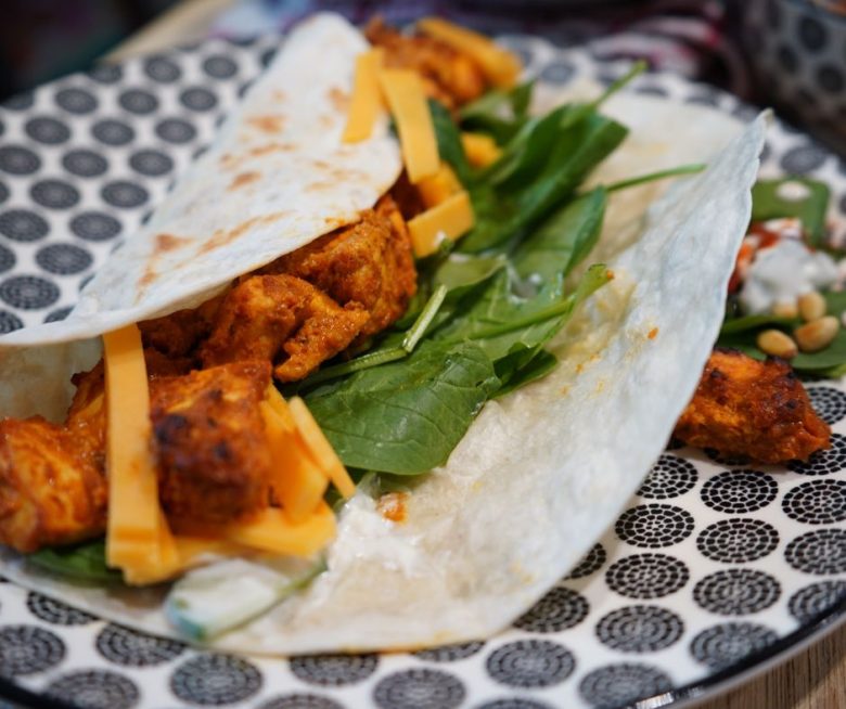 Saftiger Tandoori-Hähnchen-Wrap auf einem Teller angerichtet. Er ist gefüllt mit würzigem Tandoori-Hähnchen, Cheddar-Käse, Gurken-Joghurt-Sauce und Baby-Blattspinat