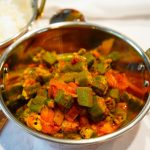 Leuchtend grüne Okras mit Zwiebeln und Tomaten in einer Kupferschale angerichtet. Das Indische Gericht heißt Bhindi Masala