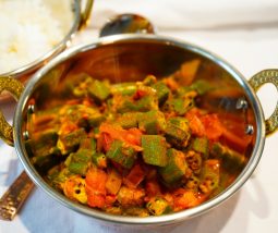 Leuchtend grüne Okras mit Zwiebeln und Tomaten in einer Kupferschale angerichtet. Das Indische Gericht heißt Bhindi Masala
