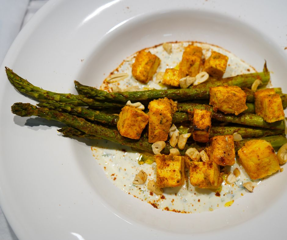 Tandoori-Spargel aus dem Ofen mit Paneer Tikka & Zitronen-Joghurt angerichtet auf einem weißen Teller, bestreut mit Cashew-Nüssen